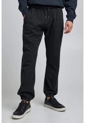 Black sweatpants made of soft fabric, featuring an elastic waist with drawstring, side pockets, and tapered cuffs at the ankles.