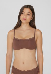 Hnědý látkový bralet s krajkovým lemem podél horního okraje a tenkými nastavitelnými ramínky, s hladkým povrchem a bezešvým designem.