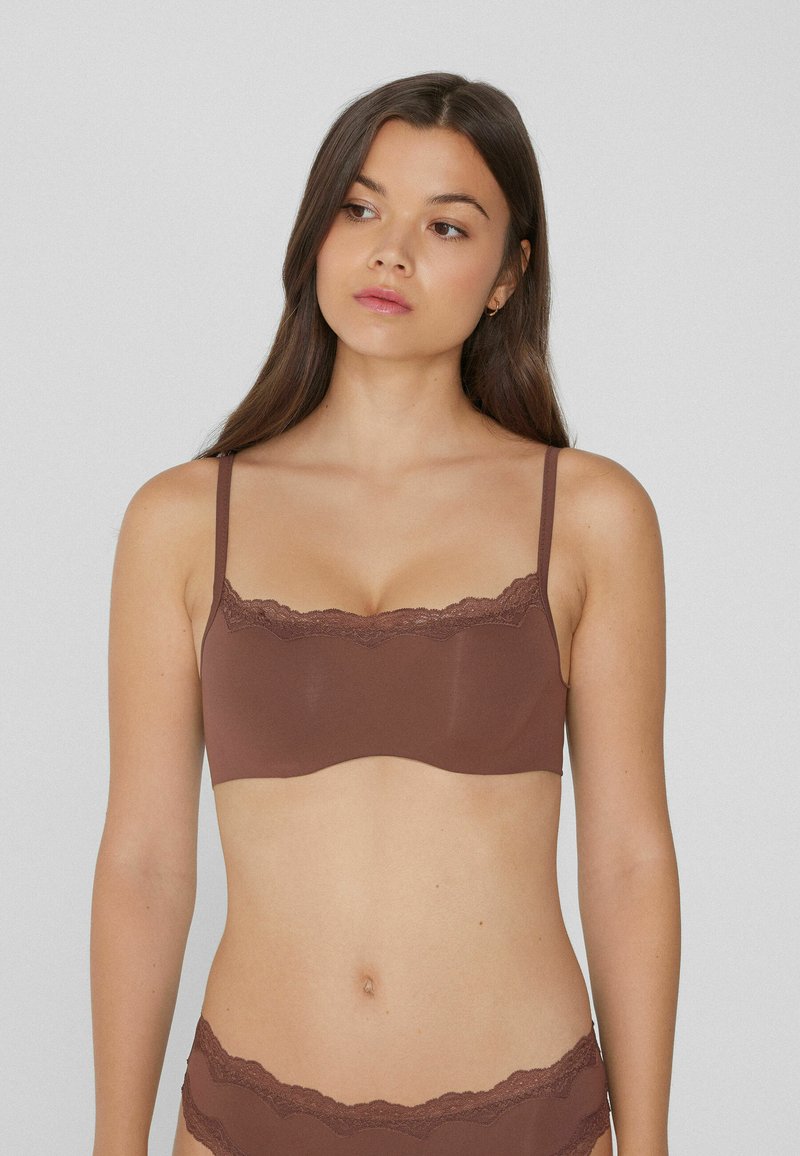 Bralette de tela marrón con encaje en el borde superior y tirantes delgados ajustables, con un acabado suave y un diseño sin costuras.