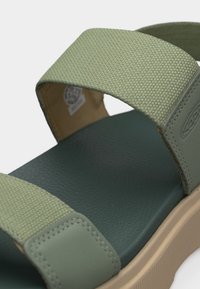 Πράσινο σανδάλι με υφασμάτινους ιμάντες με υφή και μαλακή σόλα, διαθέτοντας σχέδιο με δύο ιμάντες και μπεζ πλατφόρμα με υφή.