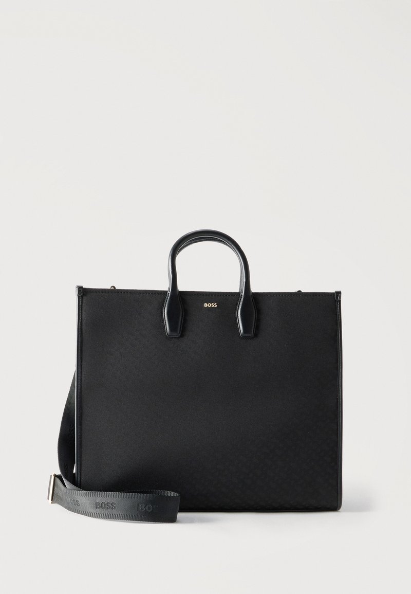Mallette rectangulaire noire avec poignées supérieures et bandoulière amovible embossée du logo "BOSS" sur fond blanc.