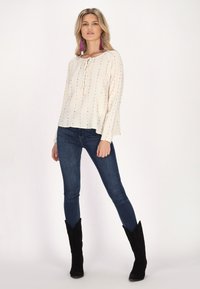 Hvid langærmet skjorte med farverig vertikal søm, en knyttet halsudskæring, parret med mørke slim jeans og sorte knæhøje støvler.