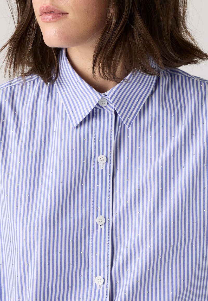 Chemise à rayures bleu clair et blanche avec un col, ornée de petites clous métalliques et d'une fermeture à boutons classique.