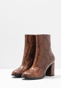 Bottes chevilles marron à imprimé serpent avec une finition brillante, talons carrés et bouts arrondis, présentant un motif de surface texturé.