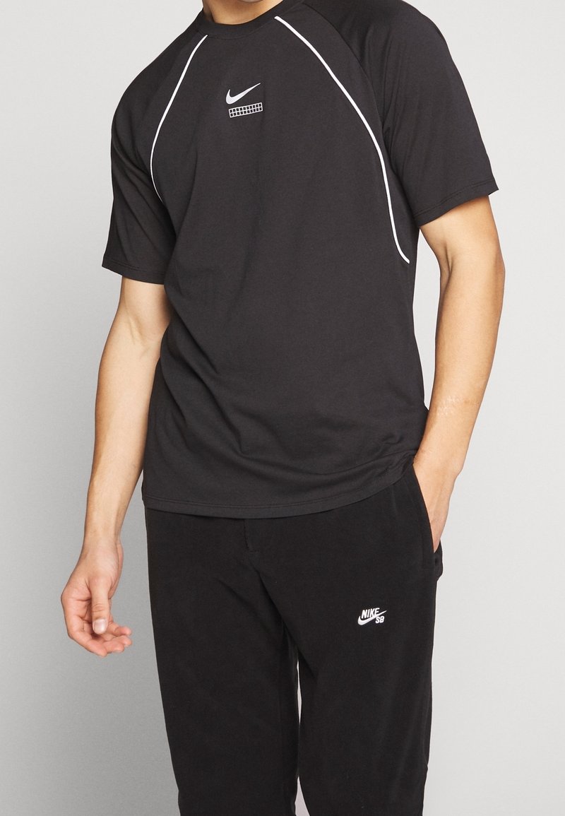 Černé tričko s krátkým rukávem od Nike s bílými akcenty, zaobleným výstřihem a logem na hrudi. Stylizováno s černými kalhotami s logem.