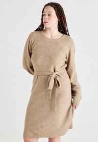 Vestido suéter de punto en color beige claro con mangas largas y cintura ceñida, que presenta un diseño de textura acanalada y un cuello redondo.