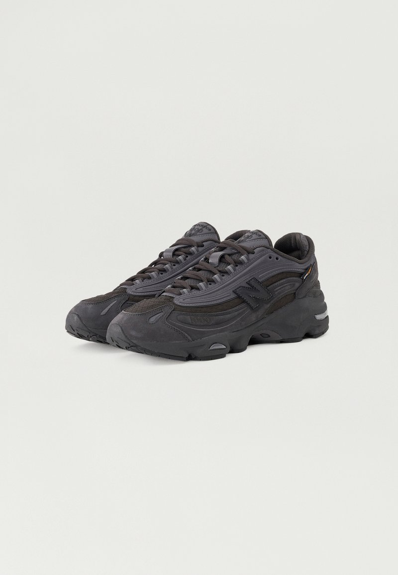 Baskets de sport noires avec un dessus texturé, présentant une semelle épaisse, des lacets et un logo sur le côté. Conçues pour le confort et la stabilité.