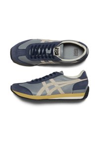 Modré a šedé tenisky s kombinací semiše a kůže. Mají bílé logo tygra, kulatou špičku a gumovou podrážku s žlutým akcentem.