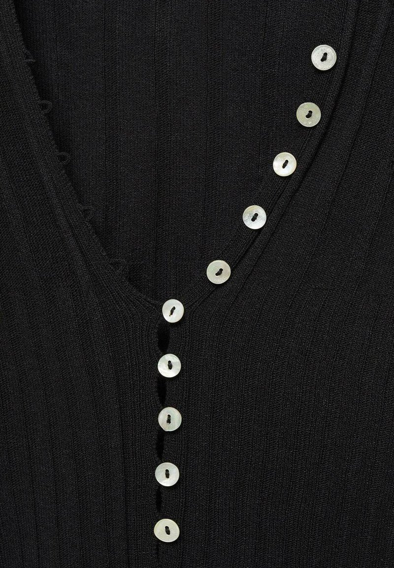 Top nero a coste con scollatura a V e una fila di sette bottoni simili a perle lungo la parte anteriore per la chiusura.