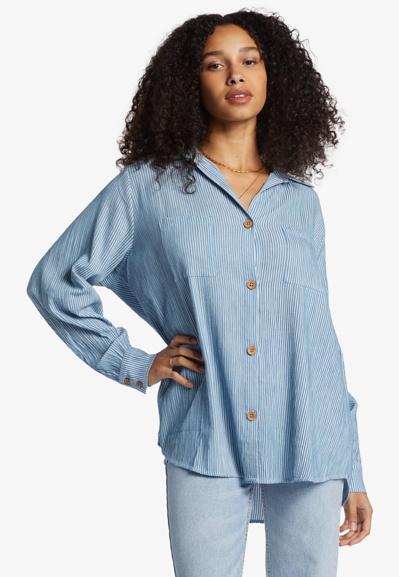 Light blue striped button-up shirt with a collar, two front pockets, and long sleeves, featuring wooden buttons and a relaxed fit.