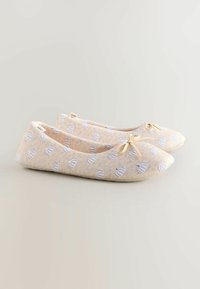 Ballettasanget er laget av beige stoff med et subtilt mønster av lyseblå skjell-lignende former. Har en liten sløyfedetalj foran.