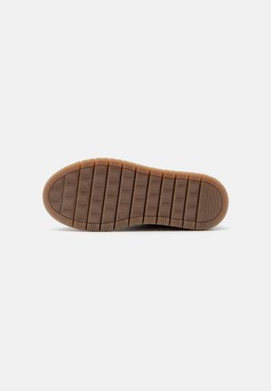 Semelle en caoutchouc marron d'une chaussure avec de profondes rainures horizontales et un motif de grip texturé, affichée à plat sur un fond blanc.