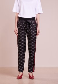 Svarta byxor med vitt prickmönster, med svart midjeband, dragsnöre och röda sidostråk. Bärs med en lös vit topp och röda skor.