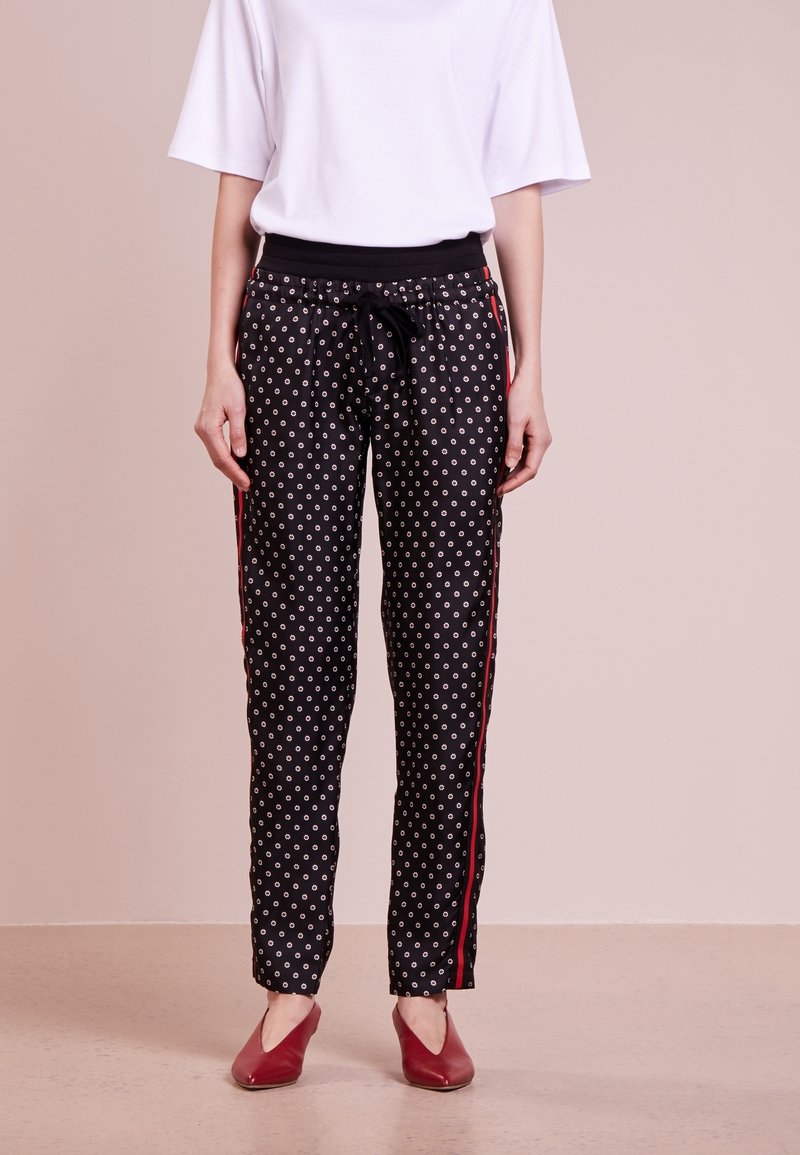 Svarta byxor med vitt prickmönster, med svart midjeband, dragsnöre och röda sidostråk. Bärs med en lös vit topp och röda skor.