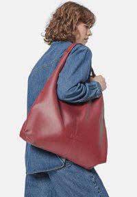 Sac à épaule en cuir rouge avec une texture galet, pr�ésentant un grand design souple et un accent logo subtil à l'avant.