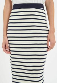 Jupe crayon tricot rayée bleu marine et blanche avec une large taille bleu marine ; longueur genou avec une forme ajustée et une texture lisse.