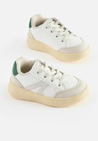 Vita sneakers med en slät läder- och mjuk mockaövre. Har en grön hälaccent, beige sula och ljusgrå snörning.