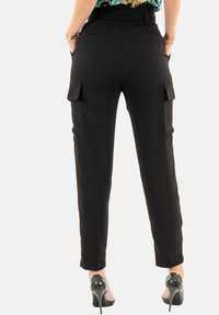 Pantalones cargo negros de corte ajustado, con dos bolsillos laterales, una textura suave y un diseño de piernas rectas. Combinados con zapatos de tacón alto.