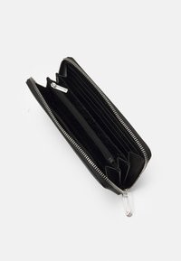 Portafoglio nero con zip, dotato di più scomparti; l'interno presenta una fodera testurizzata e un tirante della zip in argento con un accento rosso.