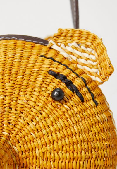 Woven straw bag in yellow, with a round shape. Features black accents and a glossy black button. Brown strap attached for carrying.