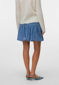 Denim krilo za skejter z ruffled robom, modre barve, v kombinaciji s kremnim pletenim puloverjem in svetlo modrimi slingback petami.