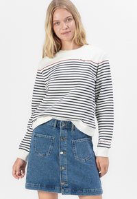 Witte sweatshirt met marineblauwe strepen en rode tekst "Happiness"; gecombineerd met een blauwe denimrok met knoopsluiting aan de voorkant en twee achterzakken.
