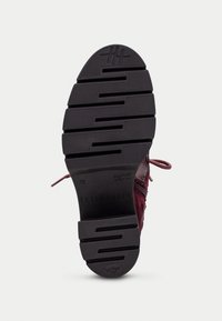 Suela de zapato con una superficie de goma negra texturizada, que presenta surcos horizontales y un logo circular en la parte superior. El color es burdeos intenso.