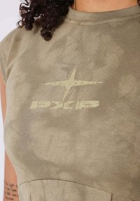 Top de color verde olivo, de manga corta y cuello redondo. La parte frontal cuenta con un logo en color claro y una sutil textura de tie-dye.