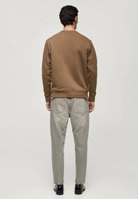 Felpa marrone con colletto e polsini a costine, abbinata a jeans grigi chiari. Modello in scarpe nere, visto da dietro.