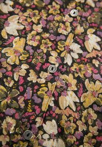 Camicia floreale con sfondo nero che presenta fiori gialli, rosa e viola. I dettagli includono bottoni rotondi e un tessuto testurizzato.