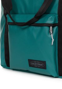 Borsa a spalla in nylon teal con manici neri, dotata di una tasca anteriore con cerniera e hardware argentato. Include il logo Eastpak su un'etichetta nera.
