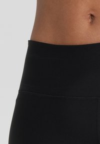 Leggings noires taille haute en tissu lisse et extensible, dotés d'une large ceinture et d'un design sans coutures sur les côtés.