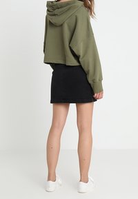 Avskuren olivgrön hoodie med huva, kombinerad med en figurnära svart jeanskjol. Vita sneakers fulländar outfiten.