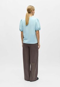 Haut bleu clair à manches bouffantes en tissu doux, associé à un pantalon marron ample et taille haute. Design minimaliste sans motifs.