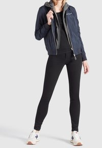 Marintröja i navy med en grå huva, svart figurnära topp, svarta leggings och vita sneakers med navy och rosa accenter.