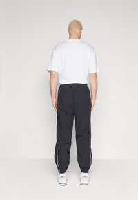 Zwarte trainingsbroeken met zijstrepen, lichtgewicht stof en een elastische tailleband, gecombineerd met een eenvoudig wit T-shirt en witte sneakers.