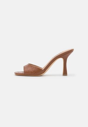 Mule en cuir marron à motif crocodile, talon haut, bout ouvert et talon aiguille fin sur fond blanc.