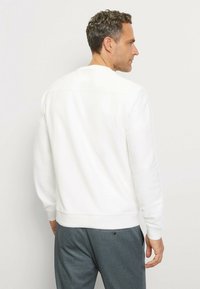 Weißer Sweatshirt mit langen Ärmeln, gerippten Bündchen und Rundhalsausschnitt. Glatte Stofftextur, kombiniert mit dunkelgrauen Hosen.