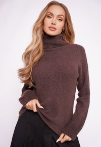 Brązowy golf z miękkiego dzianinowego materiału, z długimi rękawami, luźnym krojem i lekko skróconym dołem.