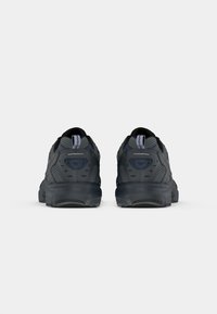 Black athletic shoes with a textured mesh upper, contrasting heel accents, and a cushioned sole, viewed from the back.