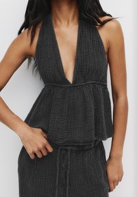Haut sans manches noir, texturé, avec un décolleté en V profond et un ourlet peplum, présentant un motif à carreaux subtil. Confectionné en tissu léger.