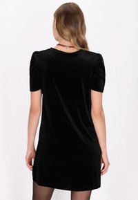 Rochie scurtă din catifea neagră cu mâneci puff, textură netedă și decolteu rotund. Caracteristici: croială lejeră și o ușoară strălucire.