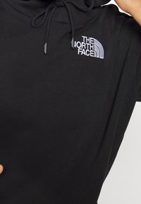 Sweat à capuche noir avec le logo blanc « The North Face » brodé sur la poitrine et des cordons visibles près de l'encolure.