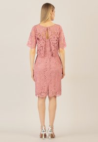 Rosa Spitzenkleid mit kurzen Ärmeln, Rückenschlitzdetail, taillierter Form, knielang und mit gewelltem Saum. Kombiniert mit silbernen Knöchelriemen-Heels.