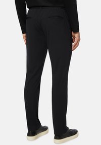 Melni stingri bikses ar elastīgu jostas daļu, divām aizmugurējām kabatām, slaidu piegriezumu un valkātas ar melnajām sporta apavām ar vieglu zoli.