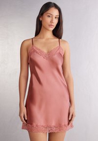 Satinowa koszulka w kolorze przykurzonego różu z regulowanymi ramiączkami, koronkowym wykończeniem przy dekolcie i hemie, charakteryzująca się gładką fakturą i luźnym krojem.