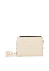 Cartera color crema hecha de material texturizado con el logo "TOUS" en relieve, cremallera dorada y un charm en forma de oso adjunto.