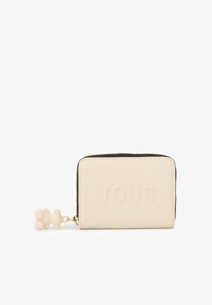 Cartera color crema hecha de material texturizado con el logo "TOUS" en relieve, cremallera dorada y un charm en forma de oso adjunto.