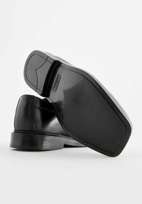 Chaussure en cuir noir vue de côté, mettant en valeur un dessus lisse, des détails cousus et une semelle en caoutchouc texturée avec un léger design angulaire.