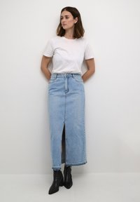 Hellblauer Denimrock mit einem Schlitz vorne, hoher Taille und ausgefranstem Saum, kombiniert mit einem schlichten weißen T-Shirt und schwarzen Stiefeletten.